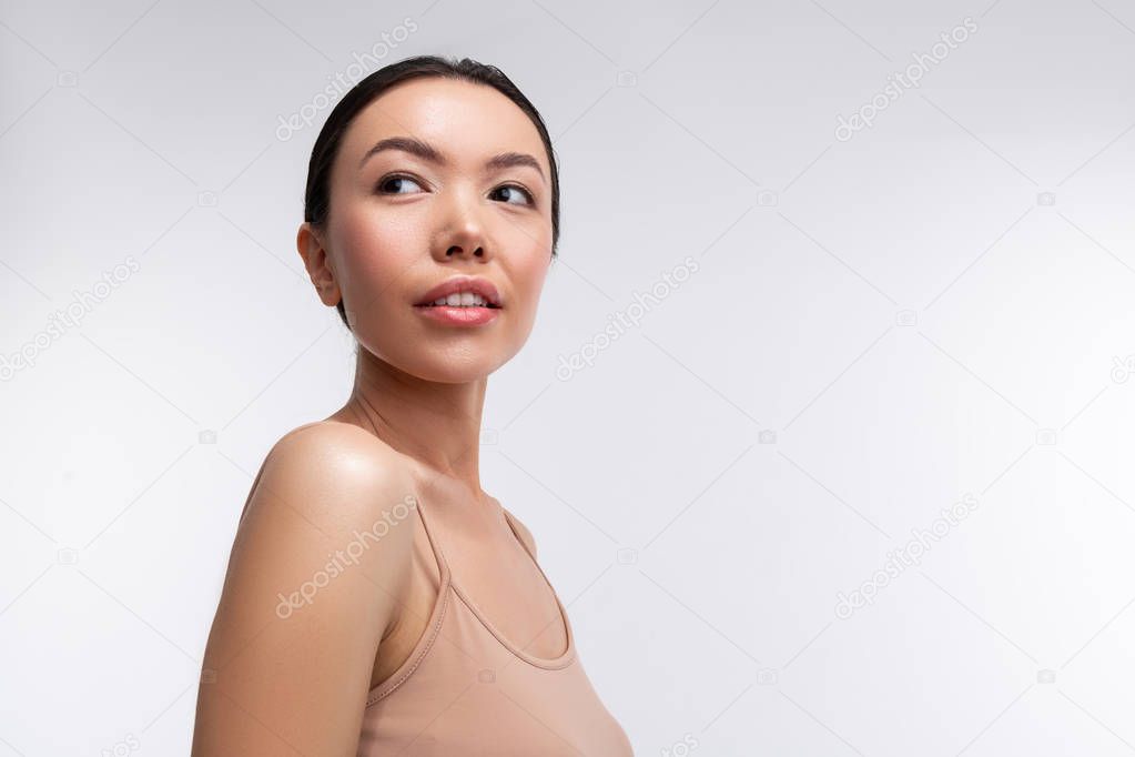 Woman wearing beige camisole standing near white background