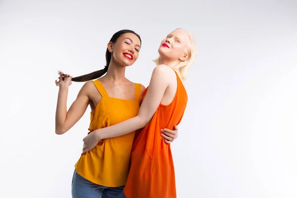 Donne con labbra rosse abbracciare mentre posa vicino sfondo bianco — Foto Stock