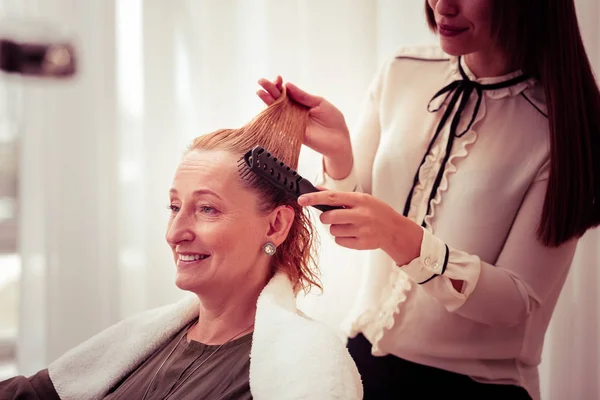 Весела перукарня розчісує волосся свого клієнта — стокове фото