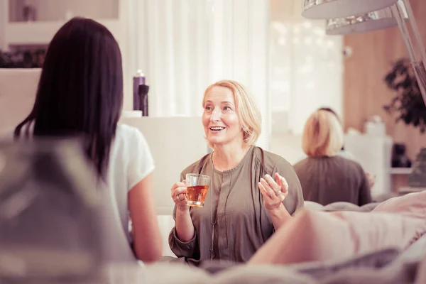 Позитивная блондинка пьет чай в салоне — стоковое фото