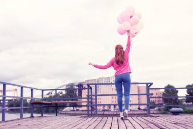 Hava balonları yığını tutan pembe parlak kapüşonlu Skinny zencefil kız