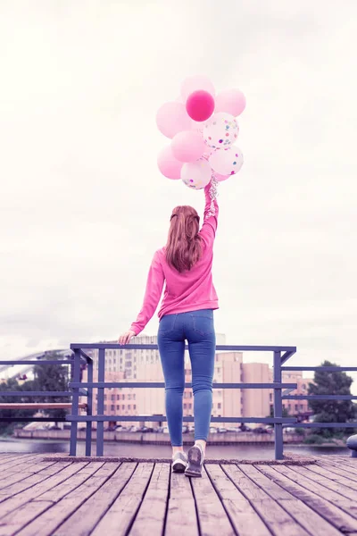 Langhaarige hübsche Mädchen mit langen Haaren tragen Bündel von rosa Luftballons — Stockfoto