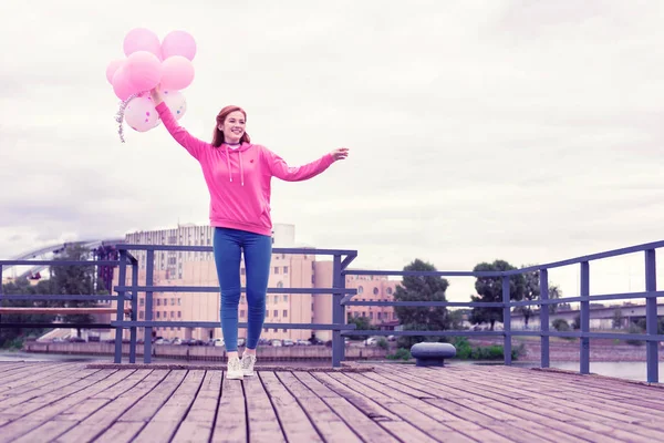 Strahlende Ingwerfrau geht mit Luftballons auf Holzsteg — Stockfoto