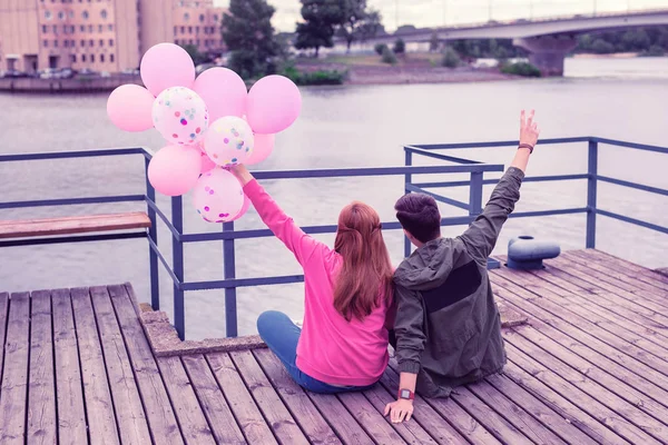 Excited young pretty couple sitting together on the river coast — Stock Photo, Image