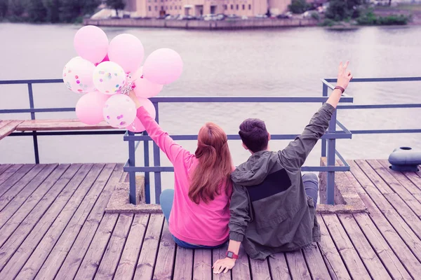 Long-haired ginger girl carrying bunch of balloons while resting on the wooden surface — Stock Photo, Image