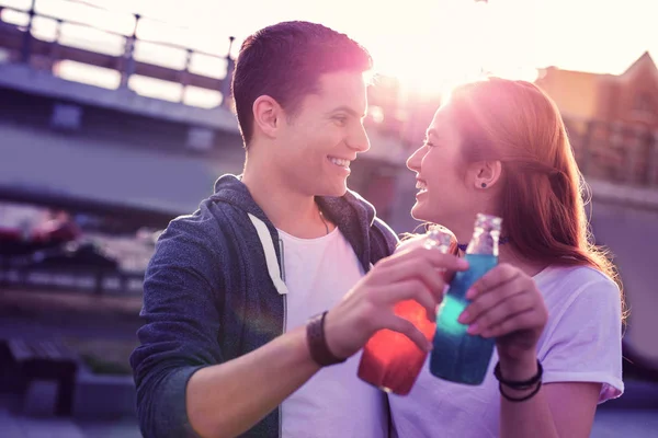 Смеющиеся позитивные молодые пары пьют освежающую газировку из стеклянных бутылок — стоковое фото