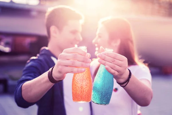 Un jeune couple séduisant debout dans des rayons de soleil chauds et portant des bouteilles — Photo