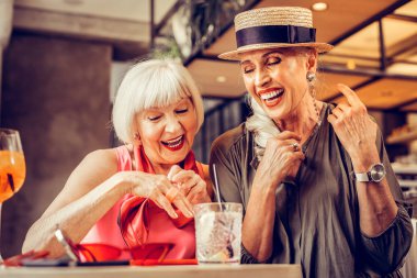 Amused good-looking old ladies being excited while drinking together clipart