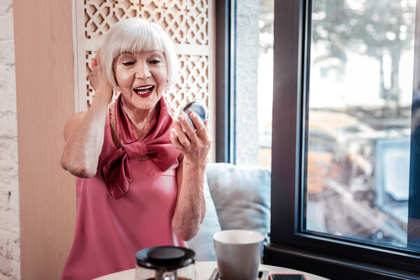 Веселая красивая пожилая женщина в шелковой блузке и с ярким макияжем
