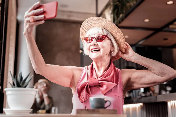 Веселая старушка в ярком макияже и красных солнцезащитных очках фотографирует себя — стоковое фото