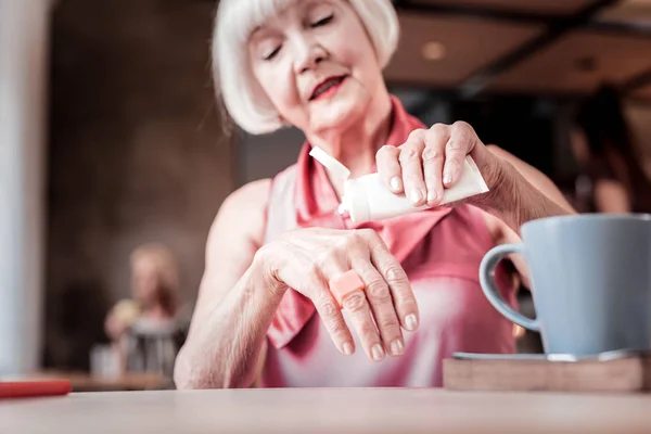 Accurate short-haired senior woman applying skincare product