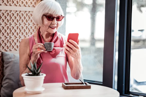 Uważna brunetka dama ubrana w stylowe okulary przeciwsłoneczne podczas wizyty w kawiarni — Zdjęcie stockowe