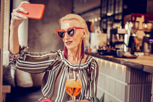 Femme âgée à la mode en forme de coeur lunettes de soleil portant smartphone rouge — Photo