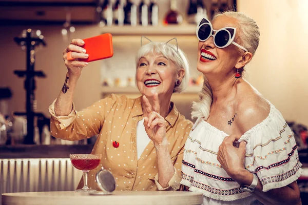 Funky moda ancianas haciendo selfie juntos mientras visitan el bar —  Fotos de Stock