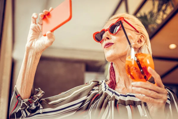 Модная коротковолосая женщина в красных солнцезащитных очках и фотографируется — стоковое фото