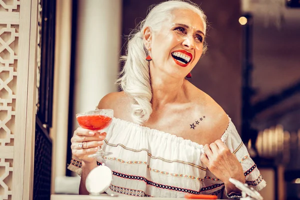 Laughing fashionable old woman showing tattoo underneath her blouse
