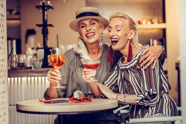 Appealing long-haired old woman hugging her blonde friend