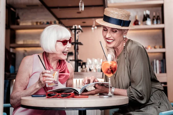 Смеющиеся симпатичные старшие подружки, сидящие вместе в кафе — стоковое фото