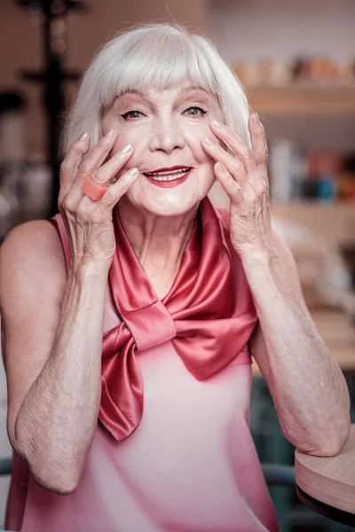 Vrolijke, goed uitziende Senior dame in zijden blouse die huidverzorgingsproducten toepast — Stockfoto