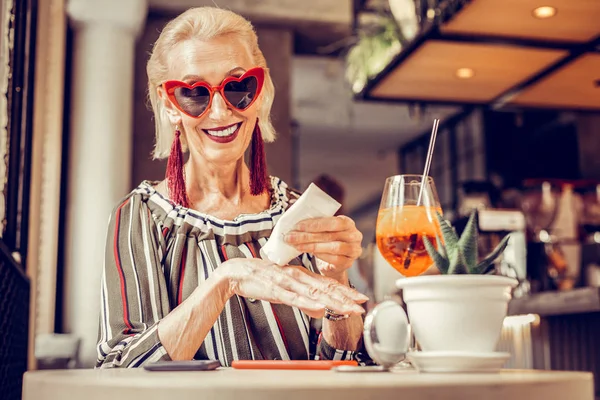 Piękna stara kobieta w funky okulary przeciwsłoneczne stosując krem odżywczy — Zdjęcie stockowe