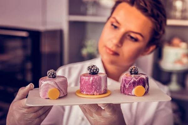 Agradable joven pastelero mirando fijamente conjunto de cupcakes —  Fotos de Stock