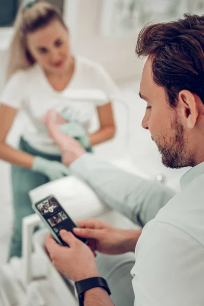 Uomo curioso dai capelli scuri che controlla il suo smartphone mentre è un maestro dai capelli lunghi — Foto Stock