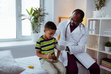 Koyu tenli çocuk doktoru enjeksiyondan önce küçük çocuğu sakinleştiriyor