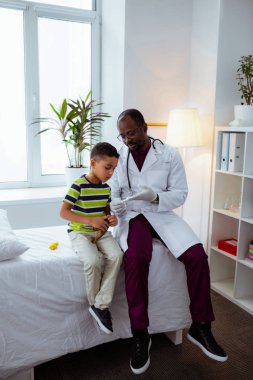 Doktor yanında oturan termometre bakarak ilgilenen çocuk hissi