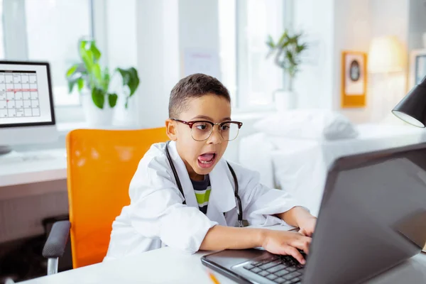 Grappig jongen het zetten van zijn tong tijdens het gebruik van laptop van vader op het werk — Stockfoto