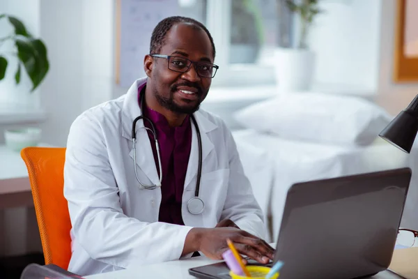 Médico afroamericano sentado en la mesa trabajando en el portátil — Foto de Stock