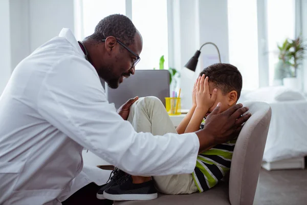 Темнокожий отец работает врачом, разговаривая с сыном, скрывающим свое лицо. — стоковое фото