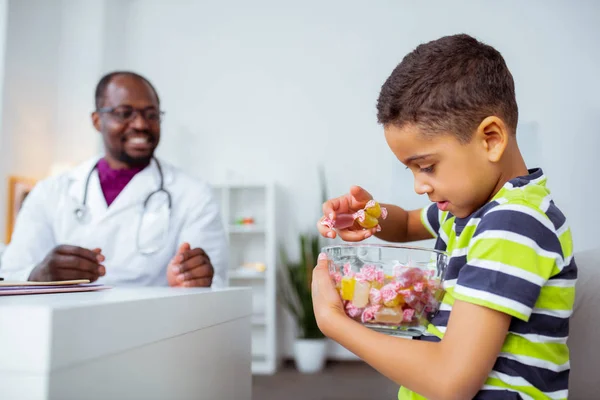 Cute funny boy holding big bowl with candies choosing one — Stock Photo, Image