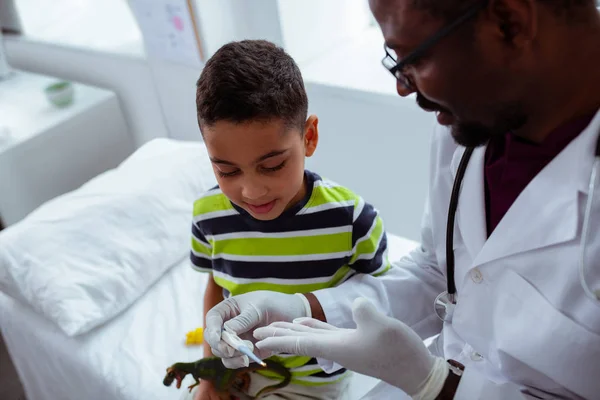 Dark-skinned children doctor showing little boy thermometer