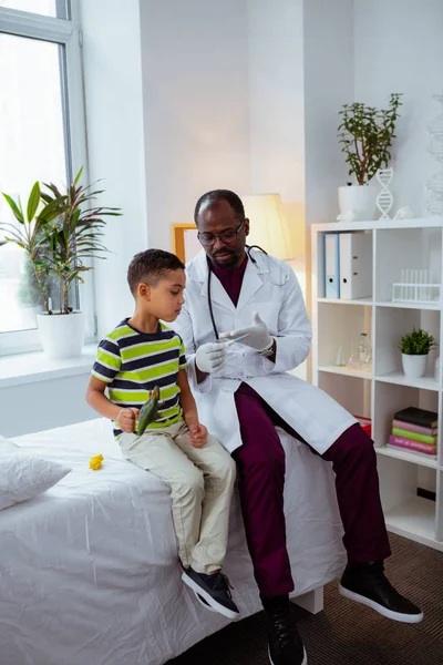 Niño jugando con juguetes sentado cerca del médico y escuchándolo — Foto de Stock