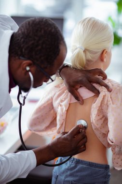 Sarışın kızın ciğerlerini dinlerken stetoskop kullanan doktor