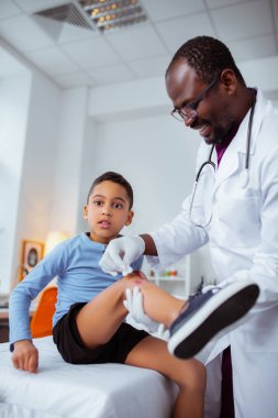 Doktor ağrılı dizini dezenfekte ederken kara gözlü çocuk acı hissediyor