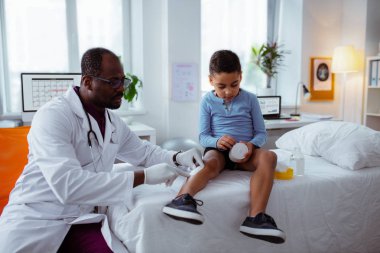 Koyu tenli çocuk doktoru küçük çocuk için bacak alçı koyarak