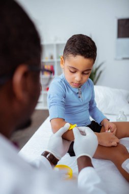 Koyu tenli doktor küçük çocuk için kol parlak alçı koyarak