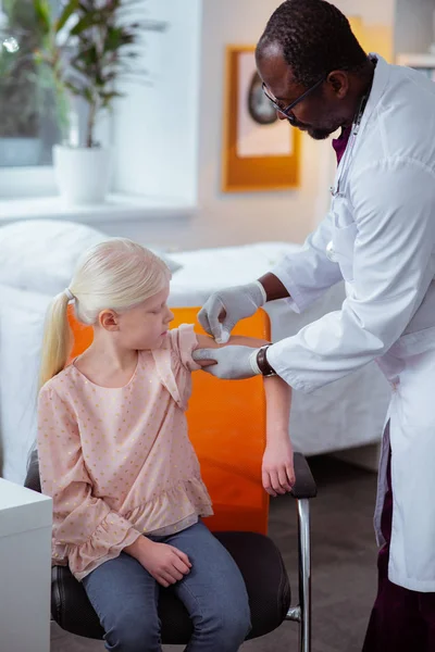 Schoolgirl sitting and watching doctor disinfecting skin after injection — Stock Photo, Image