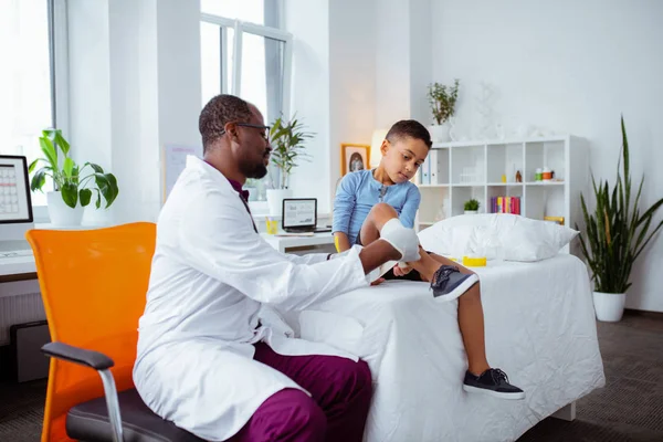 Темношкірі діти лікар дивиться на ногу маленького хлопчика — стокове фото