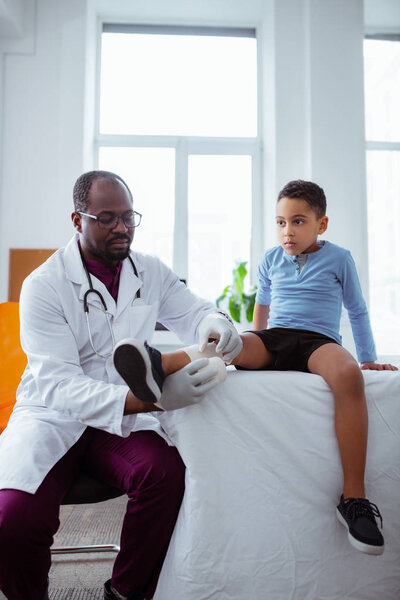 Темноволосый мальчик приходит к доктору после перелома колена
