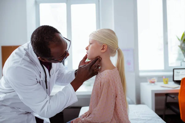 Dark-skinned doctor wearing white coat looking at throat of girl — Stock Photo, Image