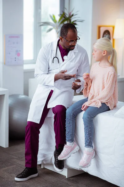 Blonde girl wearing jeans and pink blouse sitting near doctor — Stock Photo, Image