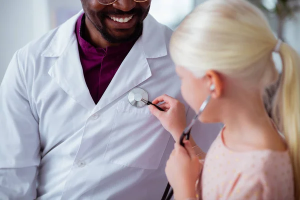Blonde patient using stethoscope playing with doctor