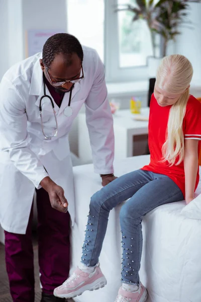 Mörkhyade barnläkare kontrollera knä av blonda snygg tjej — Stockfoto