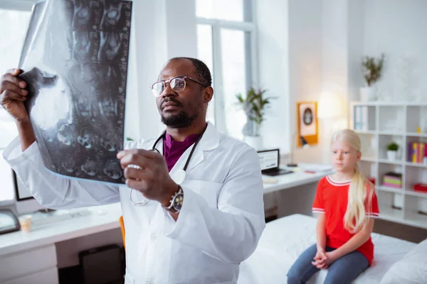 Médico de piel oscura mirando la radiografía de una linda colegiala — Foto de Stock