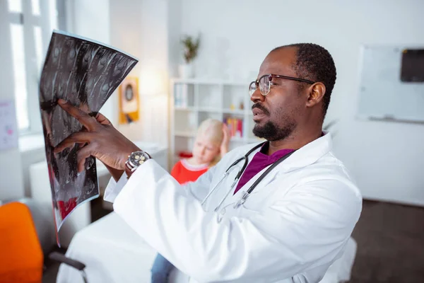 Médico barbudo mirando la radiografía de una niña rubia — Foto de Stock