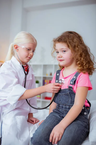 Ragazza bionda fingendo di essere medico esaminando il suo amico riccio — Foto Stock