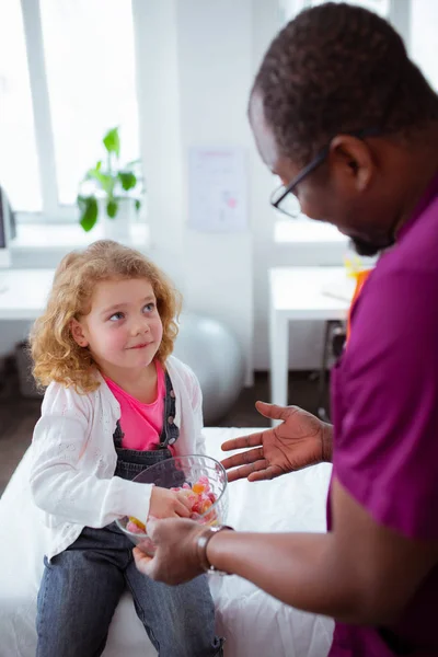 Dark-skinned doctor giving candies to cute little girl — Stock Photo, Image