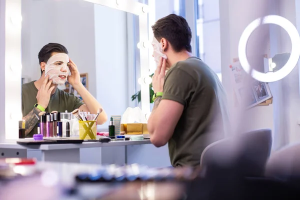 Zvědavý Tetovaný chlápek, který zkouší novou obličejovou masku, když sedí ve studiu — Stock fotografie